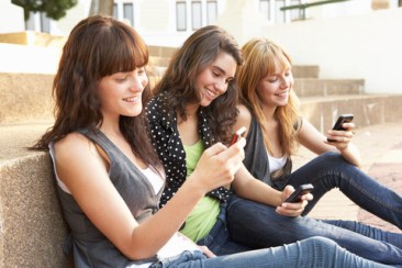 Group Of Teenage Students Sitting Outside On College Steps Using Mobile Phone